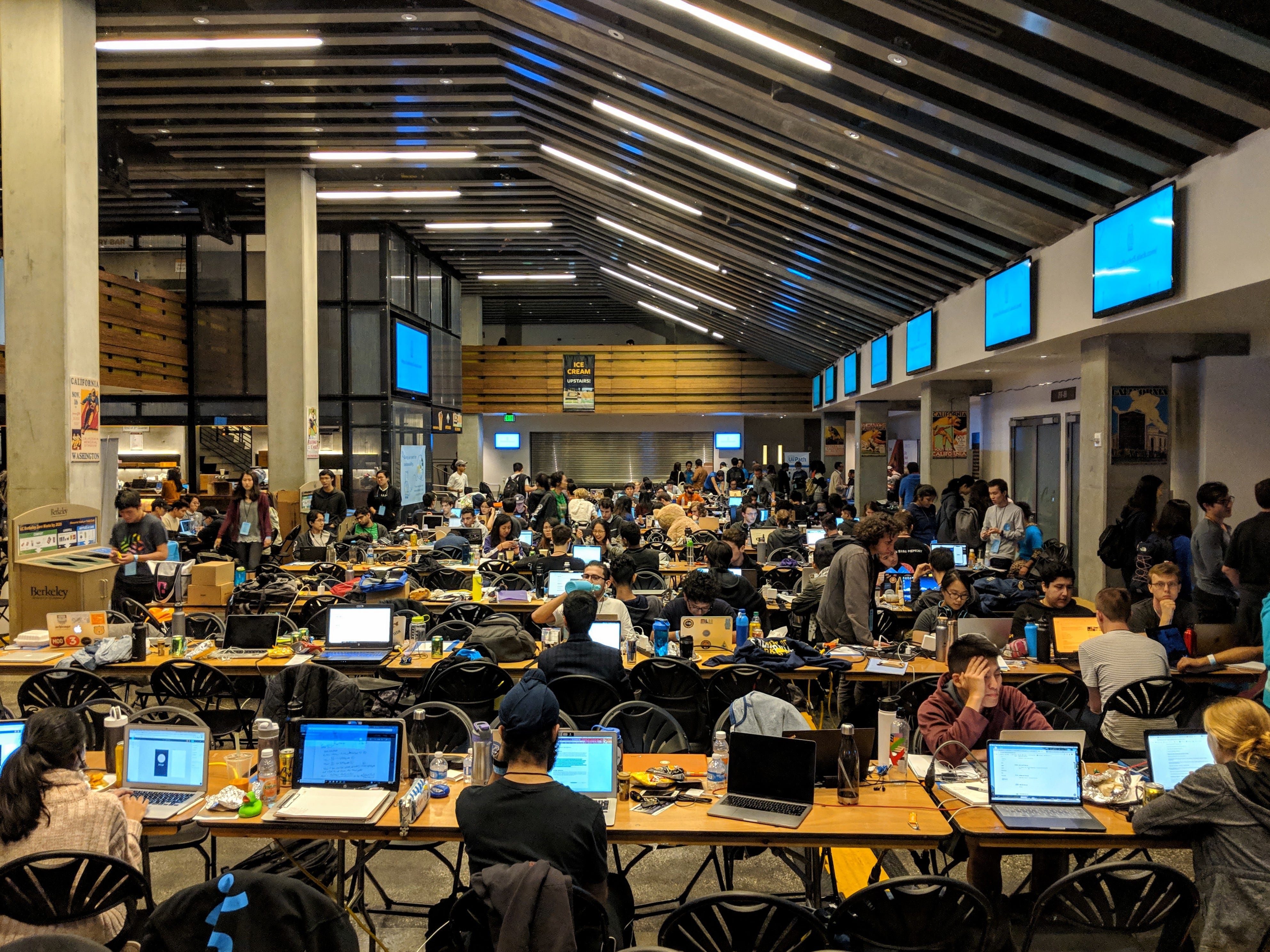 A hackathon. There are tables arranged in rows and people with laptops sitting at them.